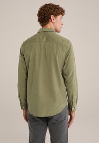 Camicia in velluto a coste verde con maniche lunghe, polsini abbottonati e orlo curvo. Presenta un yoke posteriore e una texture liscia.