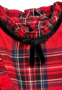 Robe à carreaux rouge avec un décolleté froncé, bordure en velours noir et un détail nœud. Les bords froncés rehaussent le design. En coton.