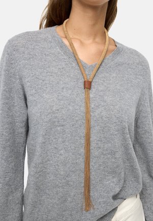 Naszyjnik w kolorze złota z długim łańcuszkiem o ażurowym splocie i brązowym skórzanym akcentem; noszony na szarym, dzianinowym swetrze z dekoltem w serek.