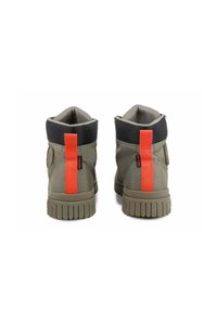 Bottes montantes en tissu vert olive avec un col rembourré noir et un accent arrière orange vif. Semelle en caoutchouc texturé avec des motifs.