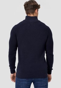 Suéter de punto en color navy con cuello alto, textura acanalada y mangas ajustadas, diseñado con un espalda limpia y de longitud media.