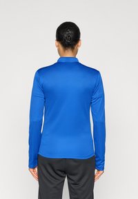 Μπλε πόλο μπλούζα με μακριά μανίκια, κατασκευασμένη από απαλό, ελαφρύ ύφασμα με γιακά. Η πίσω πλευρά έχει καθαρό σχεδιασμό χωρίς διακοσμήσεις.