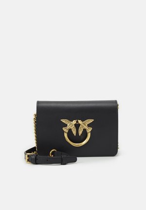 Bolso cruzado de cuero negro con correa de cadena dorada y anillo dorado decorativo con dos pájaros enfrentándose en la solapa frontal.