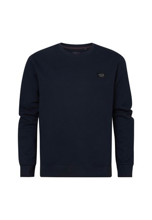 Sweatshirt bleu marine en tissu texturé. Il présente un col rond classique et des manches longues, avec un petit patch logo sur la poitrine.