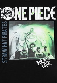 Čierne tričko s grafickým potlačou postáv so šťastnou lebkovou balónom, text znie "One Piece" a "Pirate Life" v bielej farbe.