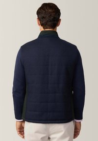 Gilet da uomo blu navy realizzato in tessuto trapuntato con una finitura testurizzata. Presenta un colletto, maniche lunghe e pannelli laterali in un colore a contrasto.