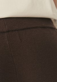 Bruine gebreide broek met een zachte textuur, met een subtiele taille naad en een aansluitend ontwerp. Gepaard met een crèmekleurige top.