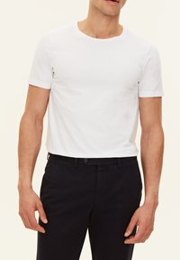 T-shirt bianca con maniche corte e scollatura rotonda, realizzata in un tessuto liscio, abbinata a pantaloni di colore scuro. Design semplice e pulito.