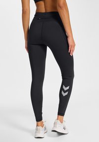 Sorte leggings med høj talje, der har et gråt chevronmønster på underbenet, lavet af strækbart materiale for fleksibilitet.