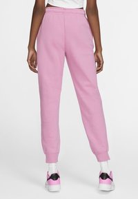 Rosa träningsoverallsbyxor med elastisk midja, ribbade anklar och en mjuk textur, matchade med vita strumpor och rosa-accenterade sneakers.