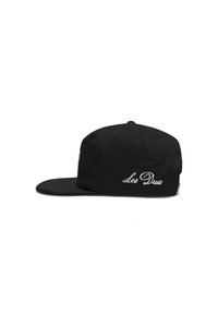 Black cap with a flat brim. Features embroidered "Les Deux" logo and button on top. Made of fabric with a smooth texture.