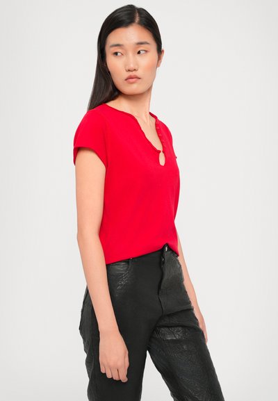Red short-sleeve top with a keyhole neckline and buttons. Worn with black textured pants, forming a simple and modern outfit.