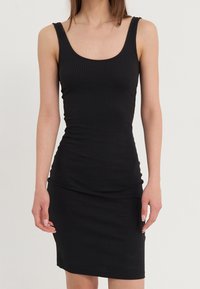 Robe bodycon noire côtelée avec décolleté en U et fines bretelles. Le tissu est extensible et doux, épousant étroitement le corps.