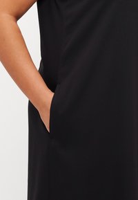 Black dress with a side pocket, made from smooth fabric. The design features a relaxed fit and subtle drape, suitable for various occasions.