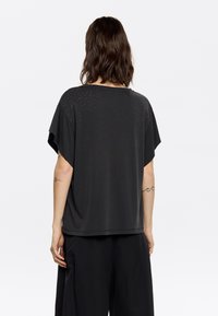 Zwarte t-shirt met korte mouwen, uitgerust met een ontspannen pasvorm, ronde hals en kleine, glanzende studs op de rug. Gemaakt van zachte, lichtgewicht stof.