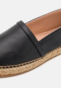 Chaussure espadrille en cuir noir avec semelle en jute tressée couleur beige et intérieur beige, présentée en gros plan sur fond blanc.