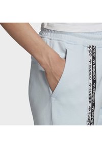 Ljust blå mjukisbyxor med en mjuk textur, med sidofickor och svart adidas-logotyp längs sömmen.