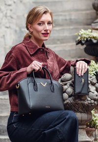 Black leather handbag with gold accents, structured shape, and two short handles. A matching black wallet with a similar gold detail is beside it.