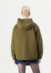 Olive green hoodie with a full hood, dropped shoulders, and elastic cuffs. Back view shows a relaxed fit and soft fabric texture.