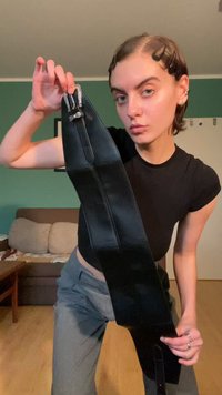 Curea din piele neagră cu un design elegant și alungit. Prezintă accesorii metalice, o textură lucioasă și detalii de cusătură vizibile.