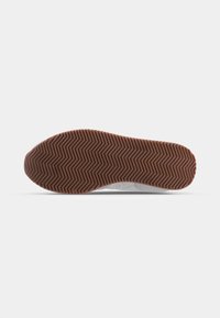 Semelle de chaussure avec motif à rayures zigzag marron sur fond blanc, vue par le dessous.