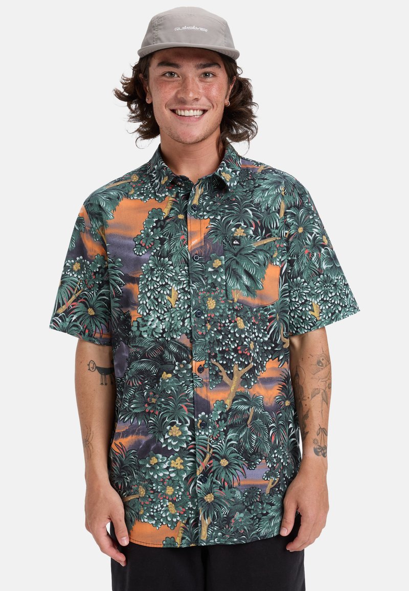 Camisa de manga corta con un colorido patrón de hojas tropicales, predominantemente verde con acentos naranjas, hecha de una tela suave y con botones.