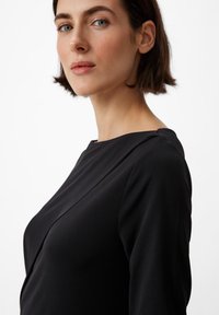 Czarna sukienka z długim rękawem o gładkiej fakturze, z dekoltem w łódkę i subtelnymi detalami na ramionach. Czysty, minimalistyczny design.