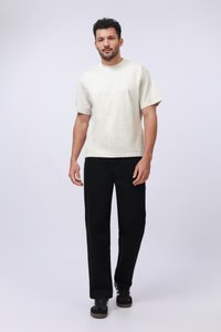 Camisa corta de manga en color beige claro con un corte relajado, combinada con pantalones negros de pierna recta y zapatillas oscuras, montada sobre un fondo sencillo.