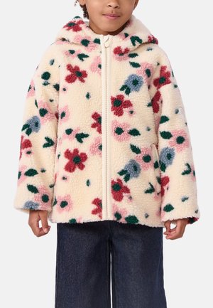 Kind trägt eine cremefarbene Fleecejacke mit einem roten, blauen und pinkfarbenen Blumenmuster und einem Frontreißverschluss über dunklen Hosen.