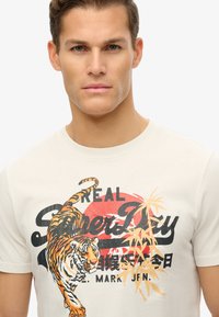 Beige cotton t-shirt featuring a graphic design of an orange tiger, black text, and red circular background with bamboo accents.