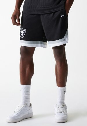 Zwarte mesh shorts met witte rand, met een Raiders-logo op de linker dij. Gecombineerd met witte sneakers en geribde sokken.