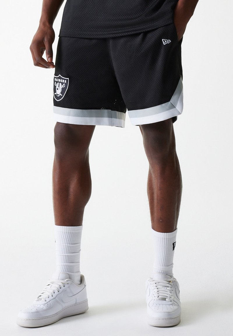 Black mesh shorts with white trim, featuring a Raiders logo on the left thigh. Paired with white sneakers and ribbed socks.