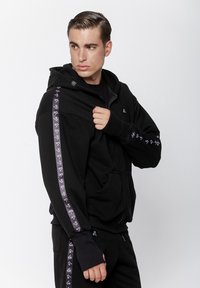 Czarna bluza z kapturem na zamek, wykonana z miękkiego materiału, z wzorzystymi akcentami na rękawach oraz logo z przodu.