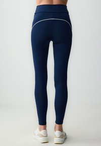 Leggings blu navy con vita alta, caratterizzati da un dettaglio di piping bianco lungo la cucitura posteriore, realizzati in un tessuto liscio e elasticizzato.