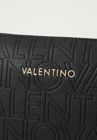 Saco de couro texturizado preto com logótipo "VALENTINO" em relevo e ferragens douradas. A superfície exibe um padrão distinto de letras.