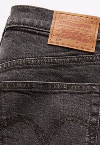 Jeans de mezclilla negra con una etiqueta de cuero marrón que presenta el logo de Levi Strauss & Co., detalles de remaches y bolsillos traseros cosidos.