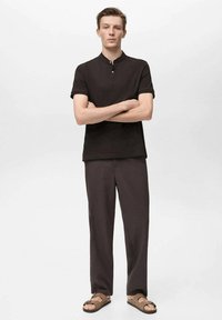 Polo shirt de culoare maro închis, cu mâneci scurte și închidere cu nasturi, purtat cu pantaloni lejeri și sandale maro. Textură netedă, design simplu.