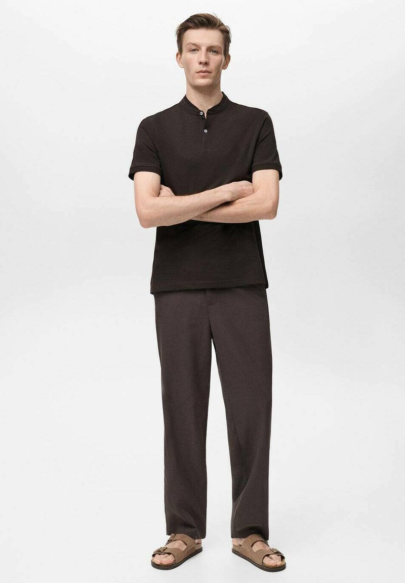 Polo shirt de culoare maro închis, cu mâneci scurte și închidere cu nasturi, purtat cu pantaloni lejeri și sandale maro. Textură netedă, design simplu.
