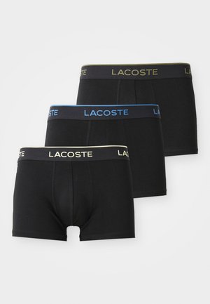 Três pares de boxers Lacoste pretos com cinturas elásticas em logótipos beje, azul e verde-oliva sobre um fundo branco.