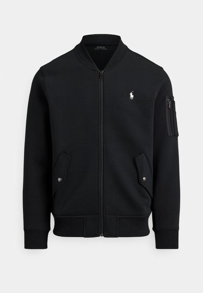 Čierna mikina na zips z mäkkej látky, s rebrovaným golierom, dvoma bočnými vreckami a vreckom na zips na ruke. Súčasťou je detail s logom.