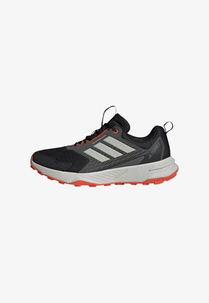 Zapatilla de trail running Adidas Terrex en negro y gris con acentos naranjas, entresuela blanca y suela texturizada para uso en exteriores.