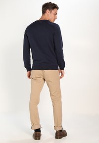 Navy Pullover mit gerippten Bündchen, getragen mit beigen Chinos. Der Pullover hat einen runden Ausschnitt und eine Slim-Fit-Passform, während die Hose an den Bündchen hochgerollt ist.
