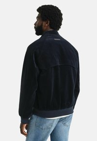 Marineblaue Cordjacke mit lockerem Schnitt, gerippten Ärmeln und einem markanten Rückenpasse. Mit einem genähten Etikett am Kragen.