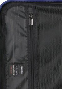 Binnenkant van een zwarte reistas met gaasvakjes, een ritscompartiment en een merklabel. Getextureerde stof met een ruitpatroon en een stijlvolle rits.