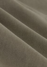 Green cotton fabric with a ribbed texture, featuring folds that create depth and shadow. The color is a muted olive green.