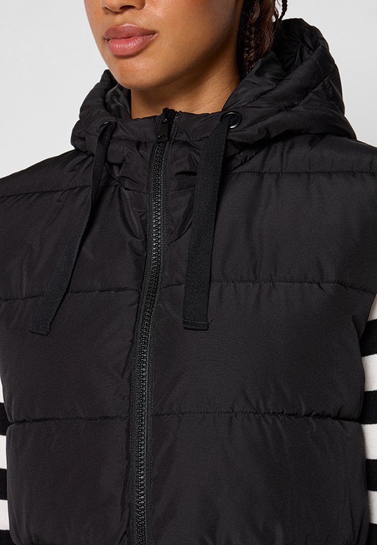 Gilet trapuntato nero con chiusura a zip e cappuccio, dotato di lacci elastici e strisce orizzontali bianche sulle maniche.