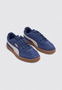 Baskets en daim bleu avec des accents beiges, bout arrondi et semelle en caoutchouc. Elles présentent un design à lacets et des panneaux latéraux texturés.