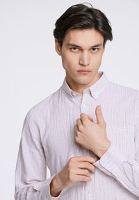 Camisa de botones de rayas blancas con sutiles líneas azules, que presenta un collar, un bolsillo en el pecho y puños abotonados.