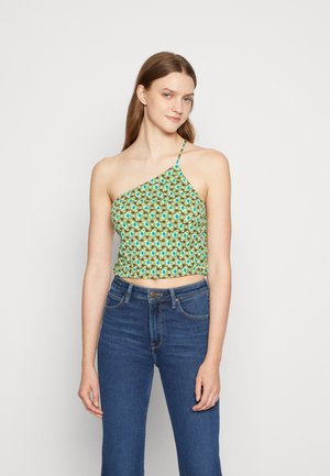 Top cropped verde com padrão e design assimétrico, apresentando uma alça única e textura franzida. Combinado com jeans azuis de cintura alta.