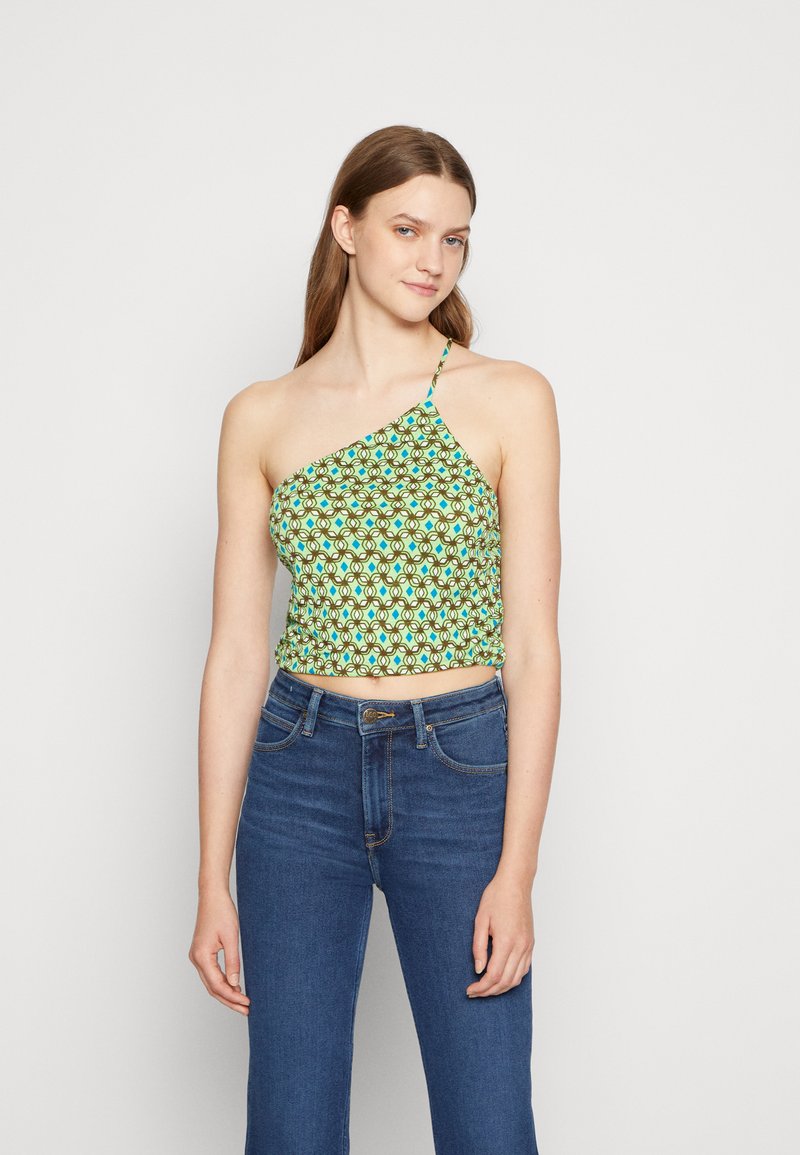 Top cropped verde com padrão e design assimétrico, apresentando uma alça única e textura franzida. Combinado com jeans azuis de cintura alta.
